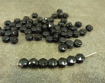 Puede incluir: Un montón de cuentas de vidrio hexagonales negras, algunas de las cuales están enhebradas en un alambre.