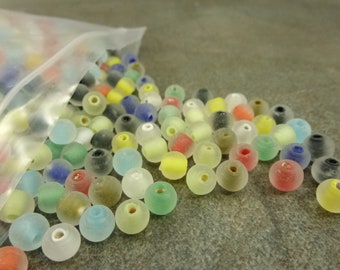 May include: A plastic bag filled with a variety of colorful glass beads. The beads are translucent and have a frosted finish. The beads are in a variety of colors, including red, yellow, green, blue, and clear.
