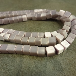 May include: A strand of light purple square beads with a shimmery finish.