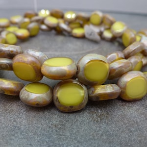 May include: A strand of yellow and brown glass beads. The beads are oval shaped with a raised, circular, yellow center.