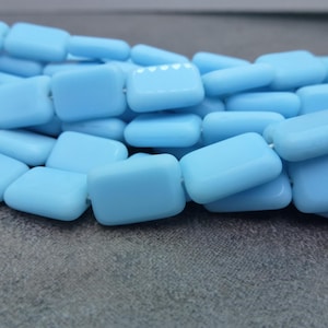 May include: A strand of light blue square glass beads. The beads are opaque and have a smooth, polished finish.