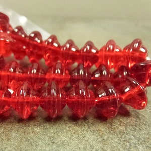 May include: A strand of red glass beads with a faceted, teardrop shape. The beads have a textured, ribbed surface.