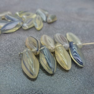 May include: A strand of translucent, light-colored glass beads with a swirl pattern in shades of blue and gray. The beads are oval-shaped and have a smooth, polished finish.