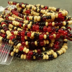 May include: A pile of red, black, and cream colored beads. The beads are small and round, and they are strung together on a string.