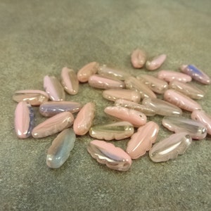 May include: A collection of pink and iridescent glass beads in a feather shape. The beads have a translucent quality and are perfect for jewelry making.
