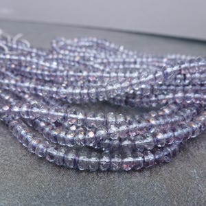 May include: A strand of faceted amethyst beads, with a light purple color and a shimmery finish. The beads are strung together on a clear thread.