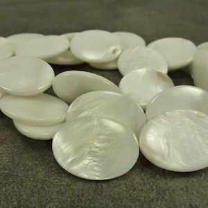 May include: A strand of white oval-shaped shell beads. The beads have a smooth, polished surface with a subtle iridescent sheen.