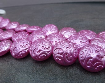 Puede incluir: Una hebra de cuentas de plástico rosa, redondas, con un diseño de espiral. Las cuentas están dispuestas en semicírculo.
