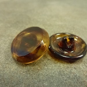 May include: Two brown plastic buttons with a shiny finish. One button has a raised center and the other is flat.