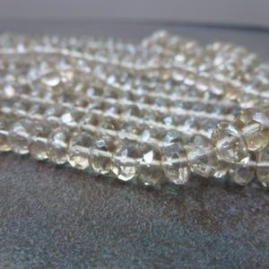 May include: A strand of clear faceted glass beads. The beads are strung on a white thread and have a slight iridescent shimmer.