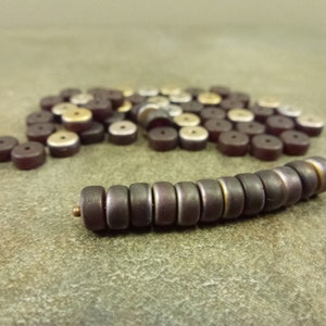 May include: A close-up of a strand of dark purple glass beads with a gold trim. The beads are arranged in a line and are scattered around the beads.