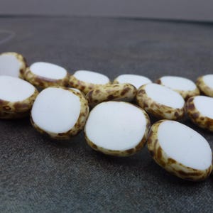 May include: A strand of white and brown oval-shaped beads. The beads have a white center and a brown speckled outer edge.