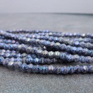 May include: Strands of iridescent blue beads with a faceted design. The beads have a metallic sheen, reflecting shades of blue, purple, and silver. These beads are suitable for jewelry making, crafting, and other creative projects.
