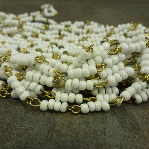 May include: A white bead chain with gold chain links. The beads are small and round, and the chain is delicate.