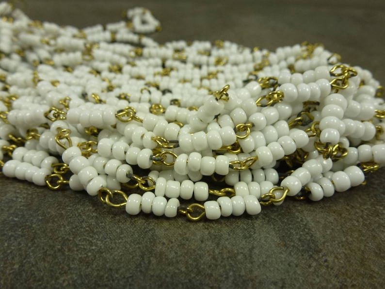 May include: A white bead chain with gold chain links. The beads are small and round, and the chain is delicate.