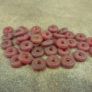 May include: A pile of small, round, dark red glass beads with a hole in the center. The beads are translucent and have a slightly frosted finish.
