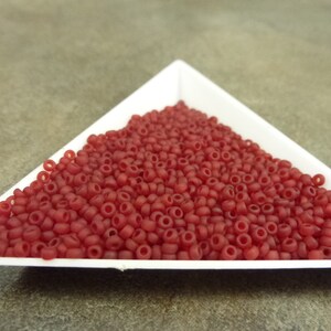 May include: A close-up of a white triangular dish filled with small, opaque, red seed beads.