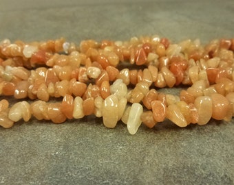 May include: A strand of orange and white chip-shaped gemstone beads. The beads are tumbled and have a smooth, polished finish.
