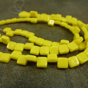 May include: A strand of bright yellow square-shaped beads. The beads are strung on a clear thread and are arranged in a circular pattern.