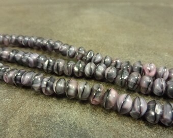 Puede incluir: Una hebra de cuentas de vidrio de color morado y negro con un patrón de espiral. Las cuentas son redondas y tienen un acabado brillante.