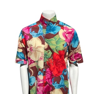 May include: A short-sleeved button-down shirt with a brown background and a colorful floral print. The flowers are in shades of pink, red, blue, and yellow.