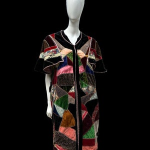 May include: A long, black velvet robe with a patchwork design. The patchwork is made of various colours and patterns of velvet, including green, red, pink, brown, and floral patterns. The robe has a V-neck and short sleeves.