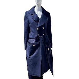 Puede incluir: Un abrigo azul marino de doble botonadura con un largo dobladillo asimétrico. El abrigo tiene un cinturón y dos bolsillos grandes en la parte delantera.