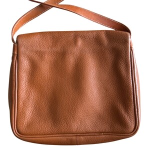 Puede incluir: Un bolso de hombro de cuero marr&oacute;n con cierre de solapa y una correa larga ajustable.