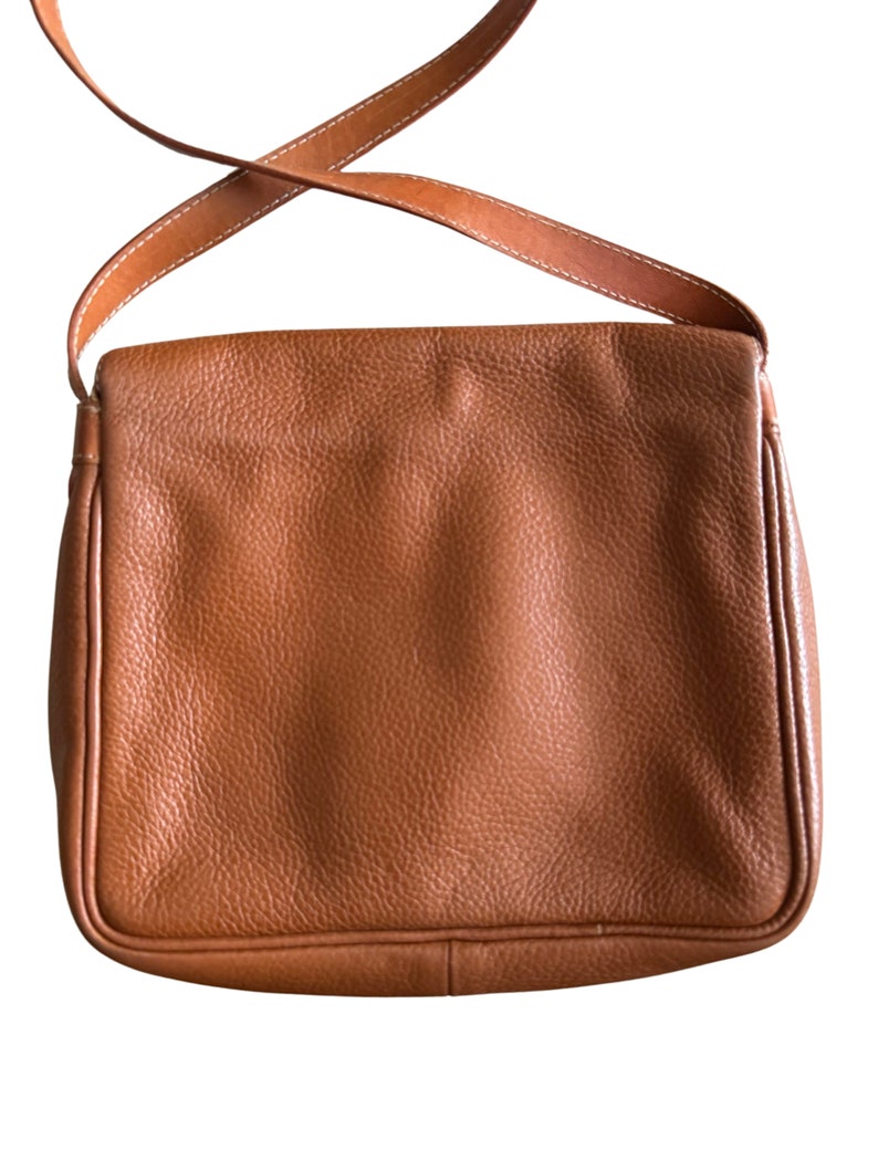 Puede incluir: Un bolso de hombro de cuero marr&oacute;n con cierre de solapa y una correa larga ajustable.
