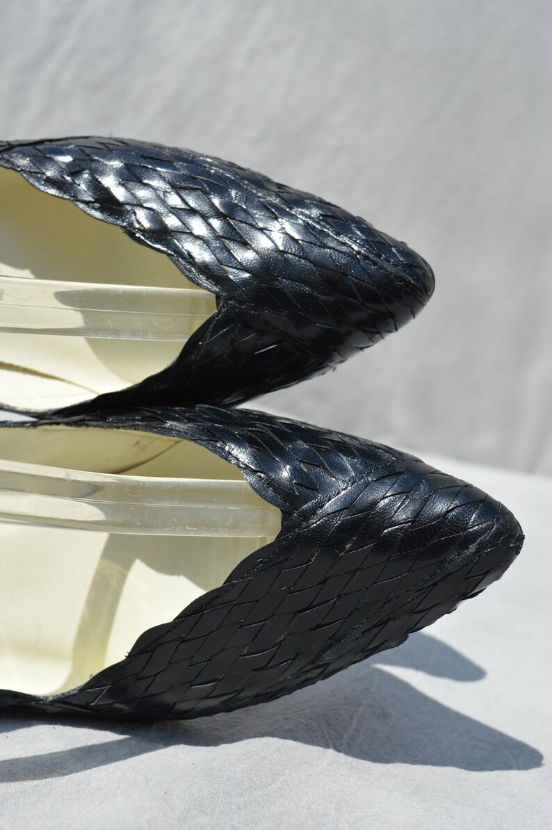 Pu&ograve; includere: Un paio di scarpe nere in pelle intrecciata con punta a punta e tacco basso.
