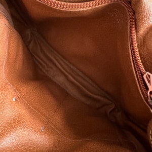 Puede incluir: El interior de un bolso de cuero marr&oacute;n con una cremallera roja. El bolso est&aacute; vac&iacute;o y el forro es de color marr&oacute;n claro.