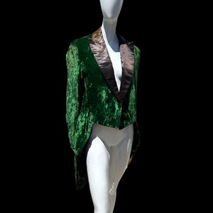 K&ouml;nnte beinhalten: Eine gr&uuml;ne Samtjacke mit schwarzem Satinkragen und einem langen Schwanz. Die Jacke befindet sich auf einem wei&szlig;en Mannequin.