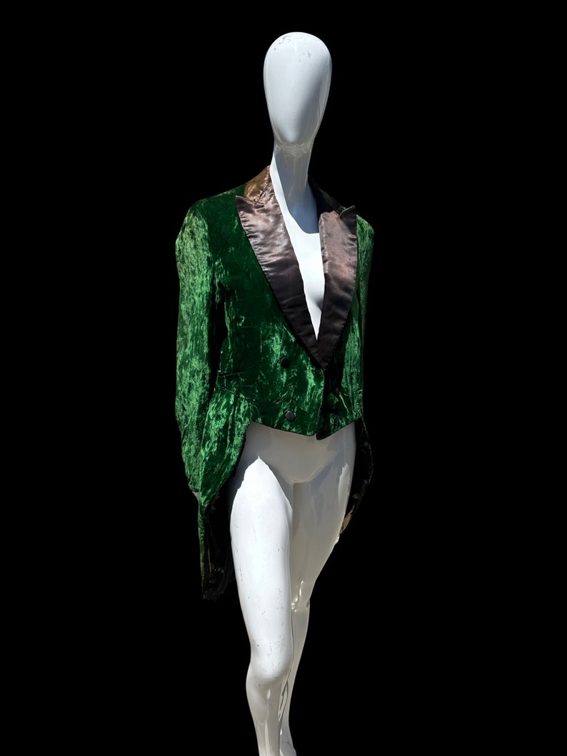 K&ouml;nnte beinhalten: Eine gr&uuml;ne Samtjacke mit schwarzem Satinkragen und einem langen Schwanz. Die Jacke befindet sich auf einem wei&szlig;en Mannequin.