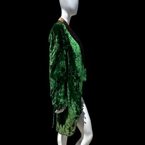K&ouml;nnte beinhalten: Eine gr&uuml;ne Samtjacke mit goldfarbenem Besatz am Kragen. Die Jacke befindet sich auf einem wei&szlig;en Mannequin.