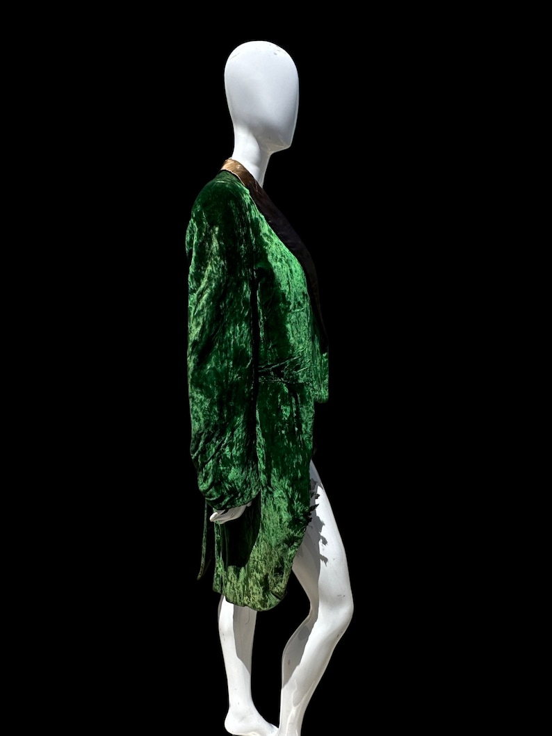 K&ouml;nnte beinhalten: Eine gr&uuml;ne Samtjacke mit goldfarbenem Besatz am Kragen. Die Jacke befindet sich auf einem wei&szlig;en Mannequin.