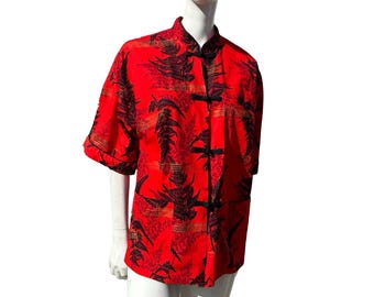 Pode incluir: Uma camisa vermelha de manga curta com estampa floral preta e dourada e gola mandarim. A camisa tem fecho de botões e é feita de um tecido leve.