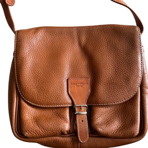 Puede incluir: Un bolso de hombro de cuero marr&oacute;n con una hebilla plateada y el texto "Courreges Paris" en la parte delantera.