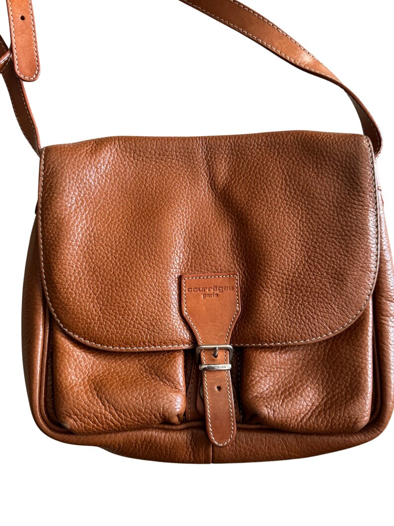 Puede incluir: Un bolso de hombro de cuero marr&oacute;n con una hebilla plateada y el texto "Courreges Paris" en la parte delantera.
