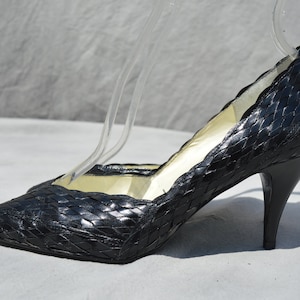 Pu&ograve; includere: Pumps in pelle nera intrecciata con punta a punta e tacco a spillo.