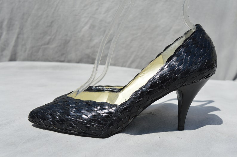 Pu&ograve; includere: Pumps in pelle nera intrecciata con punta a punta e tacco a spillo.