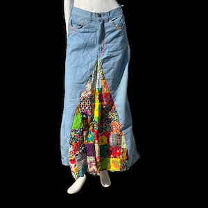 May include: Pale blue denim skirt with a patchwork design. The skirt has a high waist and a colourful patchwork panel at the bottom, featuring floral and geometric patterns. Pink stitching details are visible.