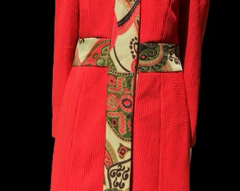 May include: A red corduroy jacket with a paisley patterned trim. The jacket has a collar and long sleeves.