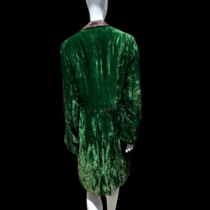 K&ouml;nnte beinhalten: Eine gr&uuml;ne Samtjacke mit schwarzem Kragen und einem langen, flie&szlig;enden Schwanz. Die Jacke befindet sich auf einem wei&szlig;en Mannequin.