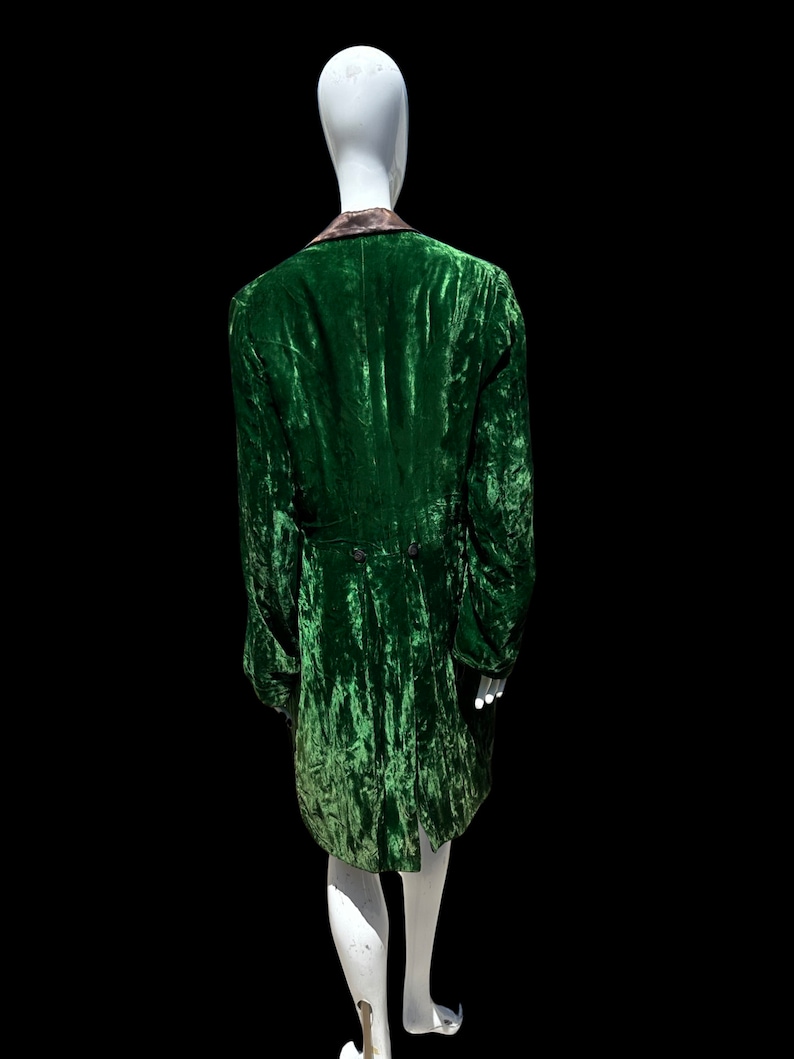 K&ouml;nnte beinhalten: Eine gr&uuml;ne Samtjacke mit schwarzem Kragen und einem langen, flie&szlig;enden Schwanz. Die Jacke befindet sich auf einem wei&szlig;en Mannequin.