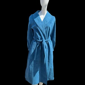 May include: A long, blue robe with a shawl collar and a matching belt. The robe is displayed on a mannequin against a black background. The robe appears to be made of a soft, textured fabric.