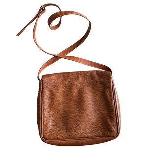 Puede incluir: Un bolso de hombro de cuero marr&oacute;n con una correa larga ajustable. El bolso tiene un cierre de solapa y una superficie lisa y texturizada.