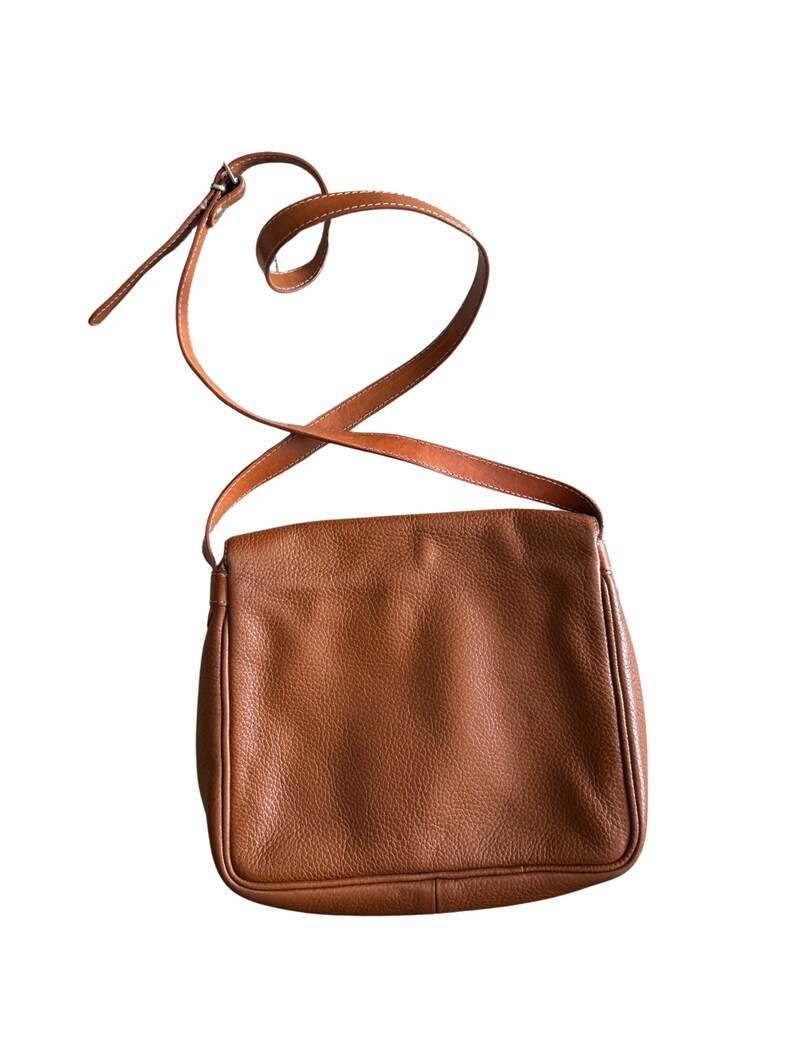Puede incluir: Un bolso de hombro de cuero marr&oacute;n con una correa larga ajustable. El bolso tiene un cierre de solapa y una superficie lisa y texturizada.