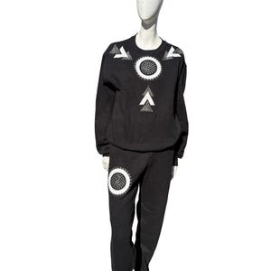 May include: Black tracksuit with white geometric patterns. The long-sleeved top has a large circle and arrow design on the front, with similar accents on the shoulders. The matching trousers feature a circle design on the left leg.