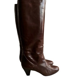 Puede incluir: Un par de botas de cuero marrón de caña alta con tacón bajo de bloque.