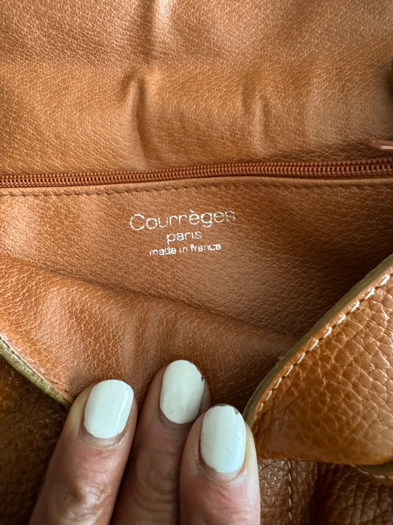 Puede incluir: Primer plano del interior de un bolso de cuero marr&oacute;n con cremallera. La etiqueta dice "Courr&egrave;ges Paris made in France".